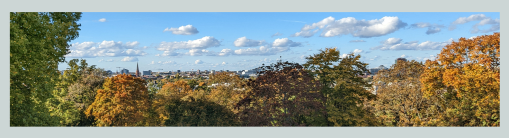 Buntes Herbstlaub, blauer Himmel mit weißen Wölkchen und in der Ferne die Skyline von Berlin